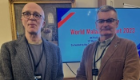 Professor Andy Waters and Professor Paul Garside stood in front of a monitor advertising the WHO report launch