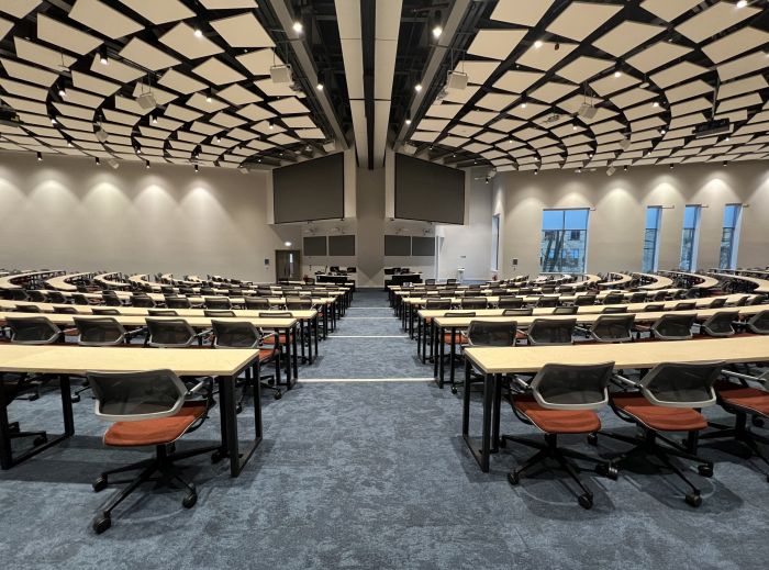 Lecture theatre with workbenches and chairs in semi-circular rows, large screens of varying sizes, and lecterns.