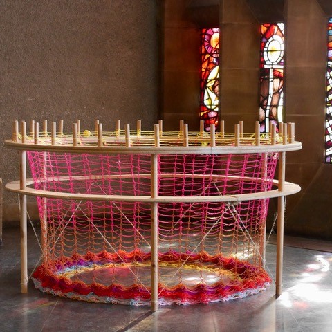 A large, circular knitting loom with light shining on it through stained glass windows.