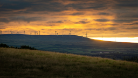 A photo of wind turbines on a hill against a vibrant sunset