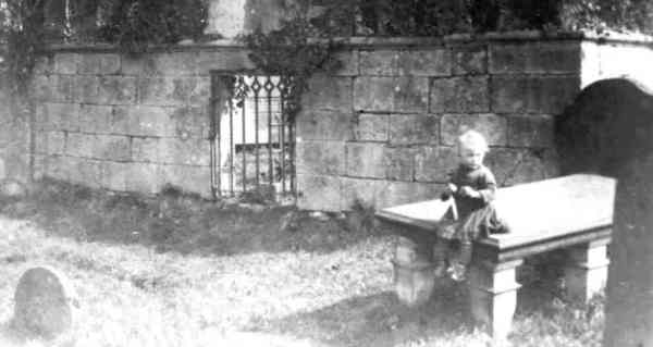 An old photo of boy sitting on a tombstone in a graveyard