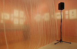 a speaker stands in the corner of a wooden platform. Translucent plastic sheeting forms two 
