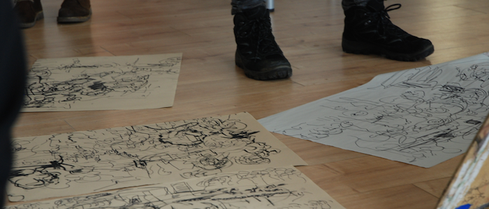 Photograph of a person's boots, standing next to drawings on the floor. Taken at 'Glasgow Kiss', A film and drawing event devised by MLitt Curatorial Practice (Contemporary Art) student Eilidh Ratcliffe, 2014 