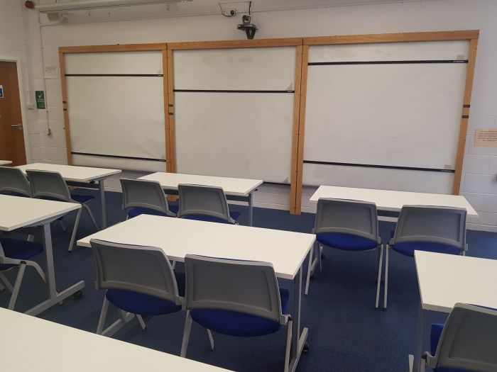 Flat floored teaching room with rows of tables and chairs, and whiteboards.