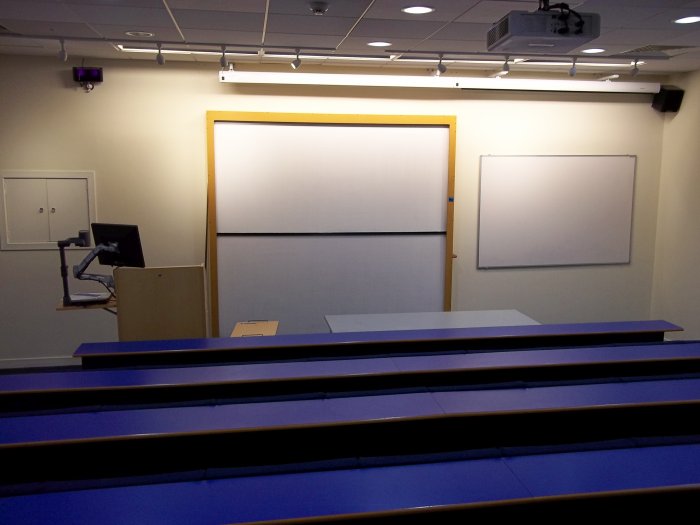 Raked lecture theatre with fixed seating, projector, whiteboard,s, screens, visualiser, and PC