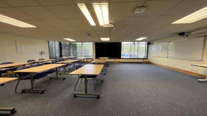 Flat floored teaching room with rows of tables and chairs, whiteboards, and projector.