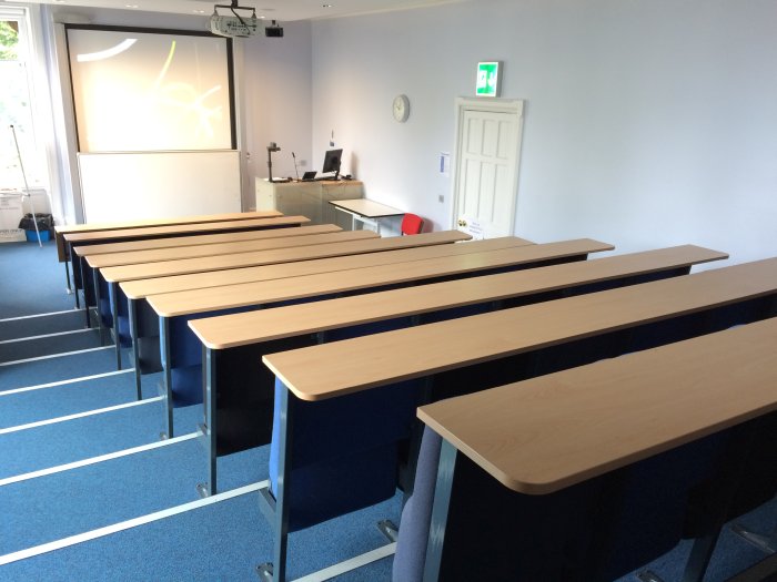 Raked lecture theatre with fixed seating, projector, screem, visualiser, and PC
