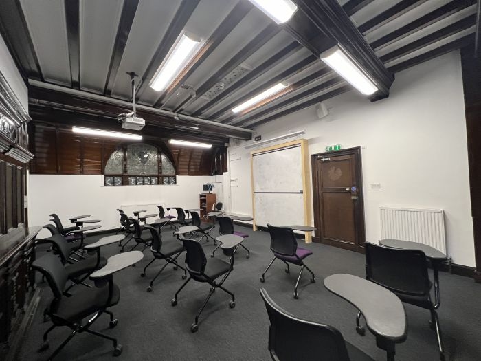 Flat floored teaching room with rows of tablet chairs, projector, whiteboard, and PC.