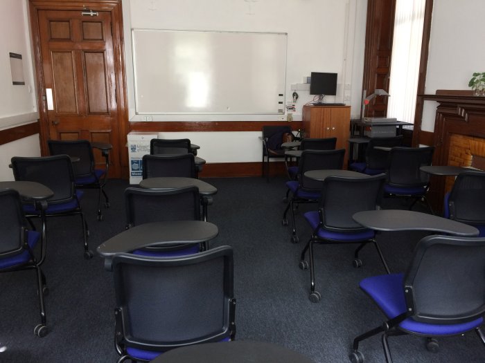 Flat floored teaching room with rows of tablet chairs, whiteboard, and PC