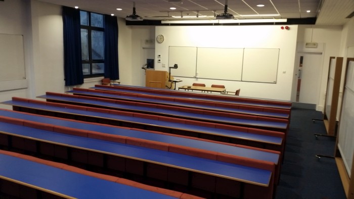 Raked lecture theatre with fixed seating, whiteboards, visualiser, and projectors