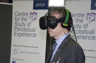 A photograph of a man wearing an Virtual Reality and Augmented Reality headset in front of banners that say 'The Centre for the Study of Perceptual Experience'.