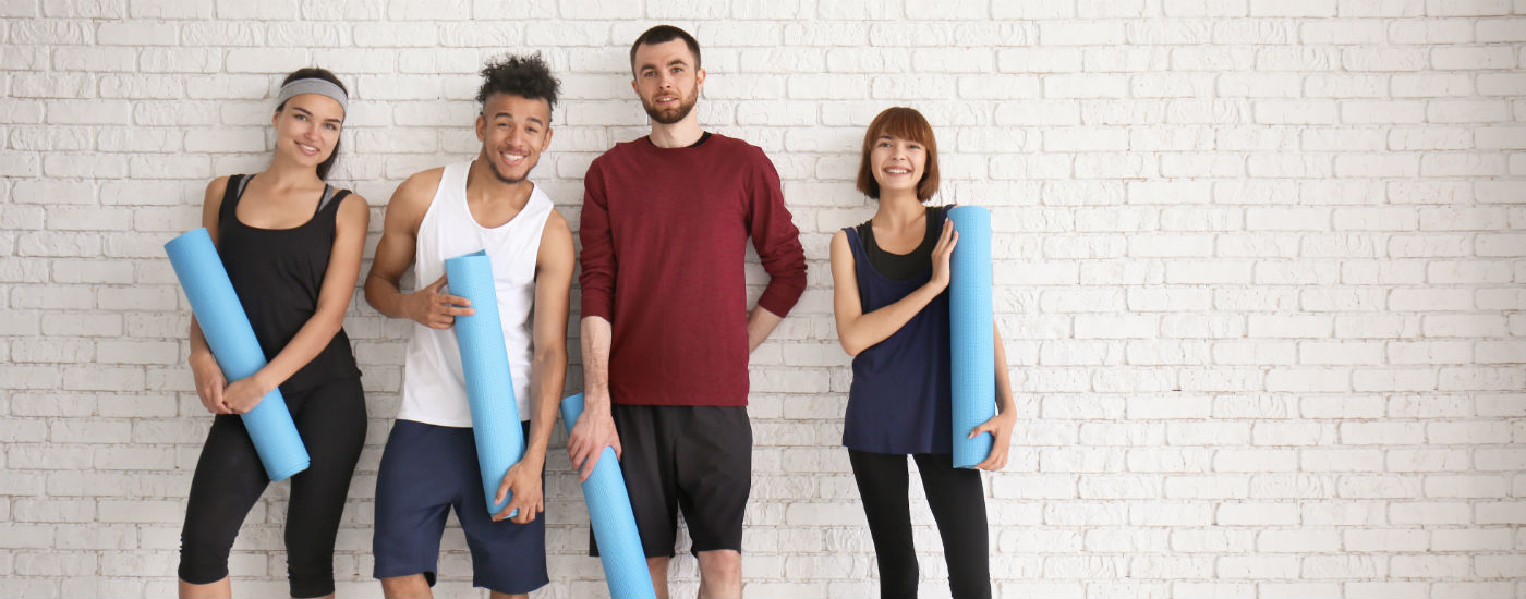 Group of gym members standing together, holding yoga mats