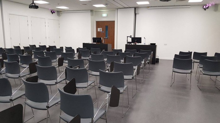 Flat floored teaching room with rows of tablet chairs, whiteboards, projector, screens, visualiser, and PC