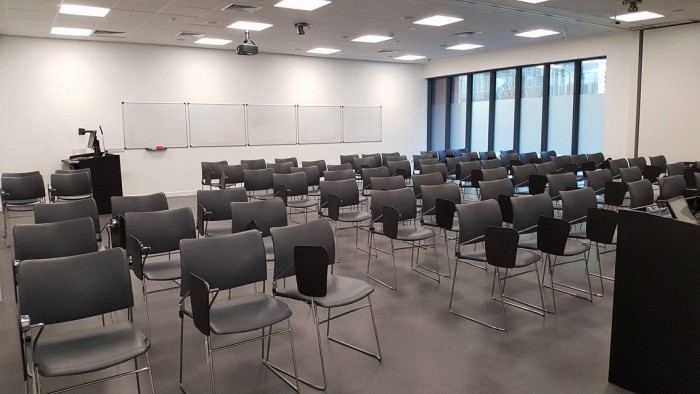 Flat floored teaching room with rows of tablet chairs, whiteboards, projector, screens, visualiser, and PC
