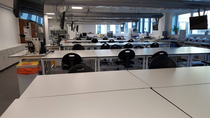 Flat floored teaching lab with large groups of tables and chairs and video monitors at each table