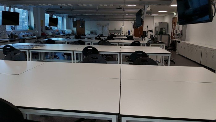 Flat floored teaching lab with large groups of tables and chairs and video monitors at each table