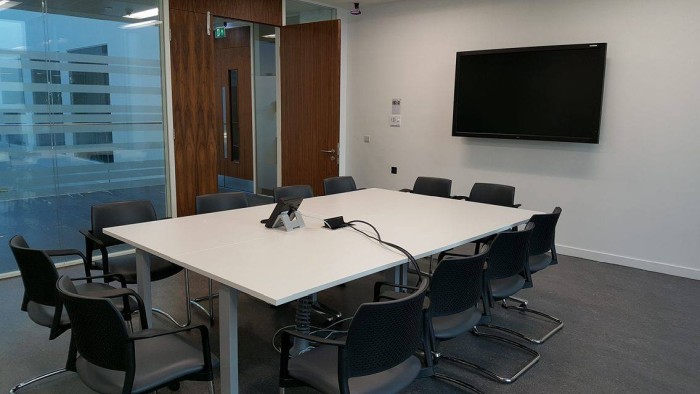 Flat floored meeting room with boardroom tables and chairs, telephone, and video monitor