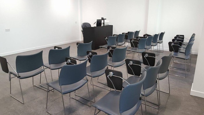 Flat floored teaching room with rows of tablet chairs, visualiser, and PC