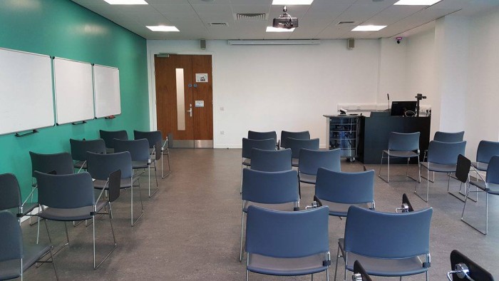 Flat floored teaching room with rows of tablet chairs, whiteboards, projector, screen, visualiser, and PC