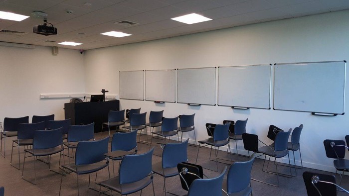 Flat floored teaching room with rows of tablet chairs, whiteboards, projector, visualiser, and PC