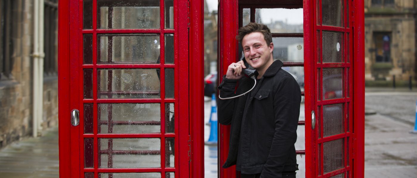One student caller making a phone call outside the main gates on the red pay phone boxes 