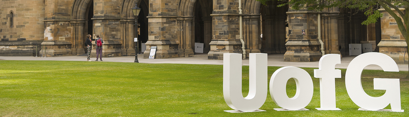 UofG letters in the West Quadrangle of the Main Building with the cloisters in the background