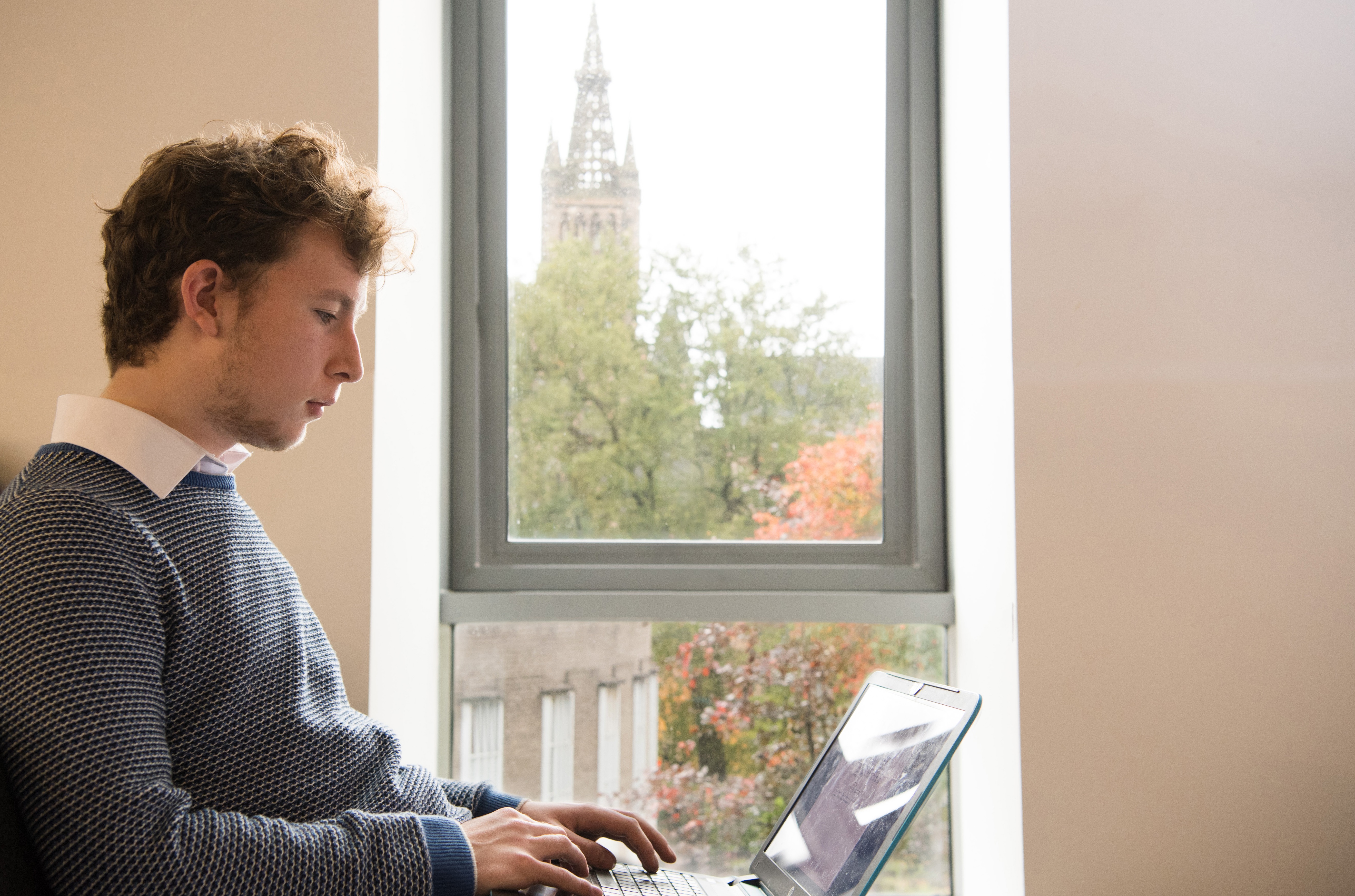 Student on laptop in front of window framing university tower