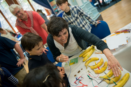 Photograph showing a child with a GSF volunteer creating an electrical circuit out of wires and bananas. 