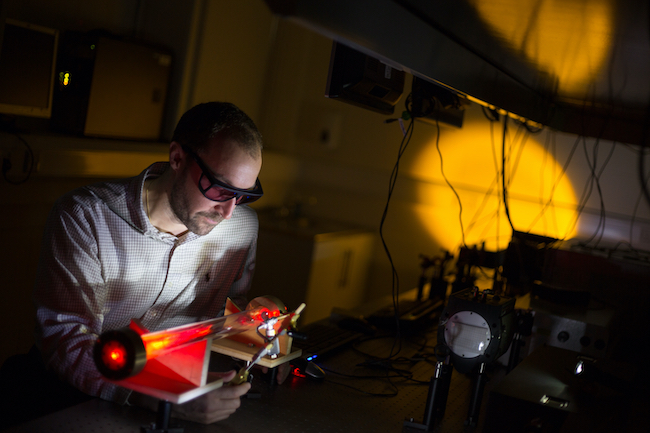 Prof Daniele Faccio examines an optical experiment on a lab bench while wearing a pair of safety glasses.