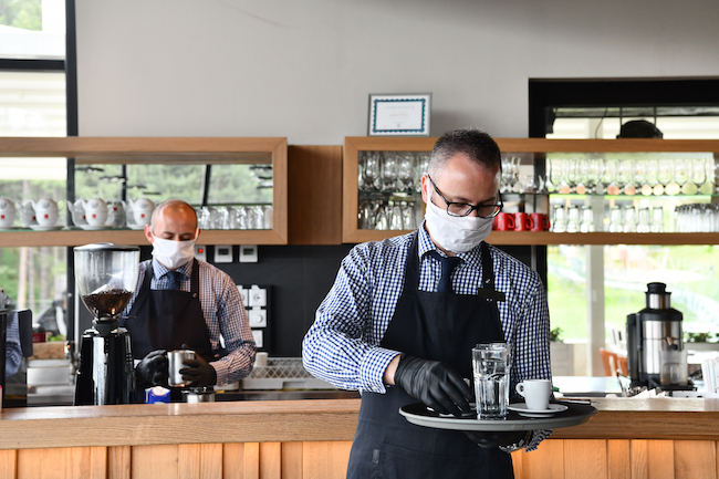 Two masked and gloved waiters work inside a restaurant during the COVID-19 pandemic