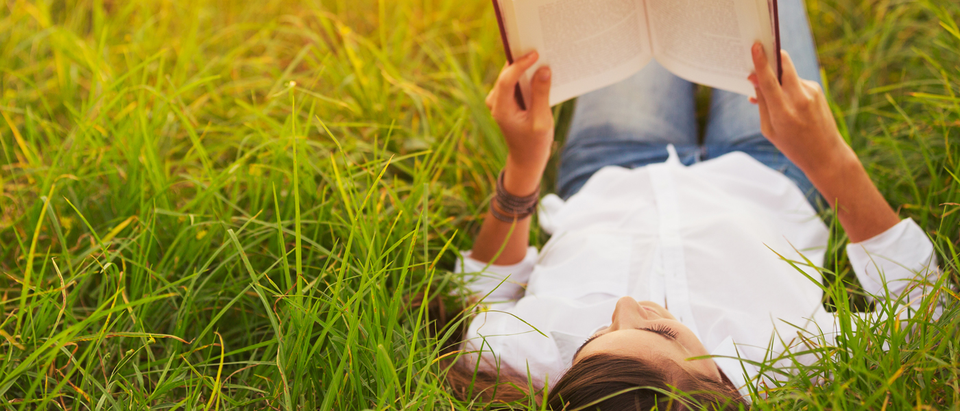 A woman lying on the grass reading a book [Photo: Shutterstock]