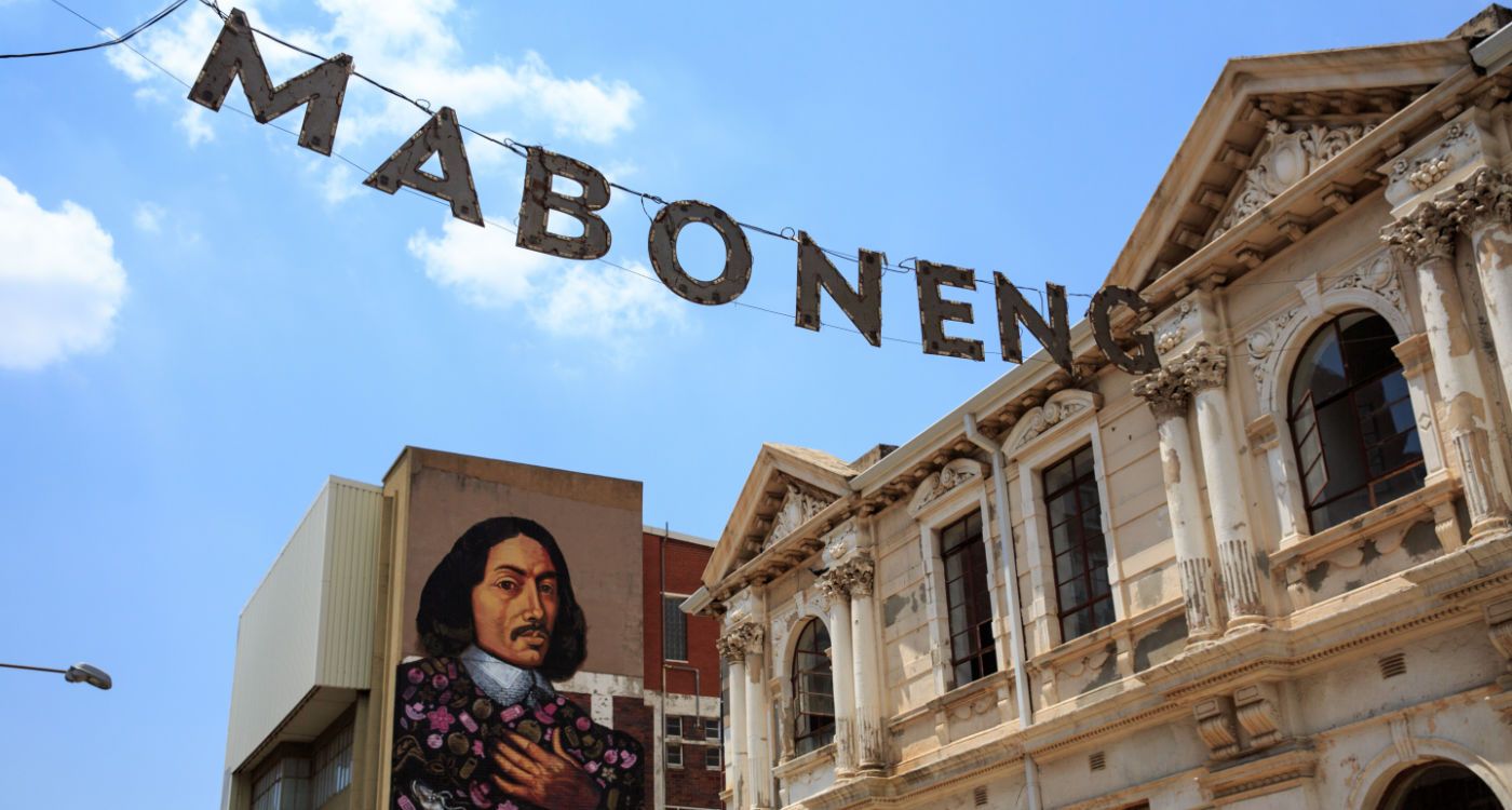 Letters spelling out Maboneng strung across a street in the district, with a large mural of a man painted on an end gable in the background [Photo: Shutterstock]