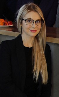 Female wearing glasses and a black suit faces the camera