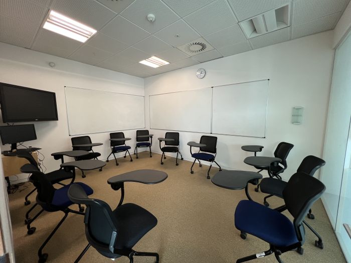 Flat floored teaching room with tablet chairs, whiteboards, video monitor, and PC.