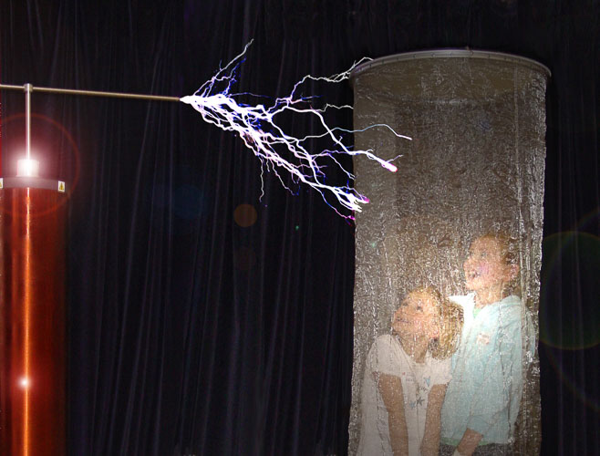 Photograph showing two children in a wire cylindrical cage whilst an electronic rod above them is making bright sparks like lightning. 