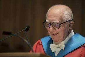 Older man wearing glasses and robes standing at lectern 