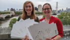 Dr Laura McCaughey and Dr Anna McGregor stood holding paper certificates fanned out with London behind them