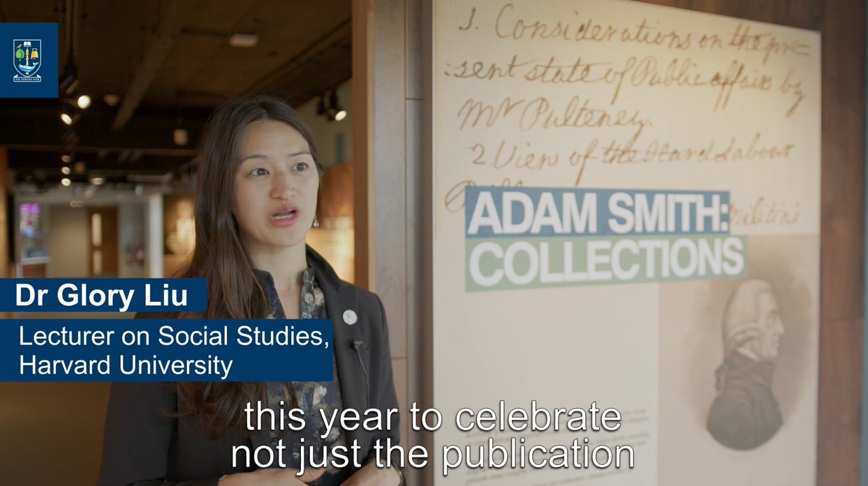 Dr Glory Liu, Lecturer on Social Studies at Harvard University speaking about Adam Smith. The speech captions read 'this year to celebrate not just he publication' She is standing next to a portrait of Adam Smith and a sign saying 'Adam Smith: Collections'