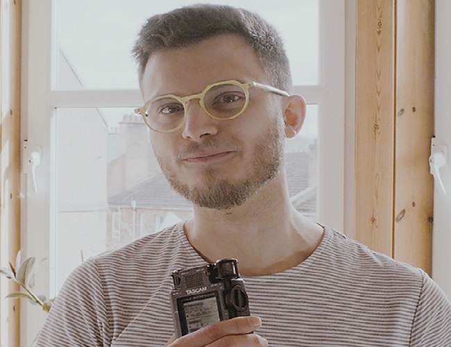 An image of a man wearing a stripped top holding a recording device. 