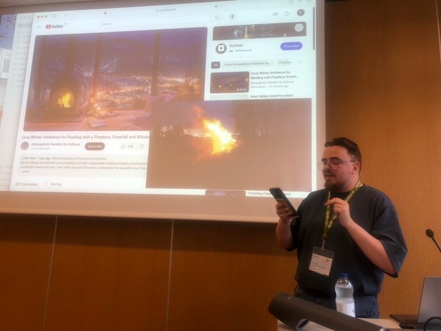 Photo of a man presenting about seasonal cultures in front of a projection of a yule log