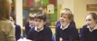 Primary age children in a classrom smiling as they listen to a teacher