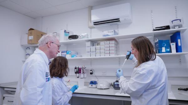 One male and two females wearing white lab coats in a discussion in a laboratory.