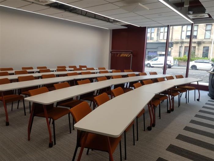 Flat floored teaching room with rows of tables and chairs.