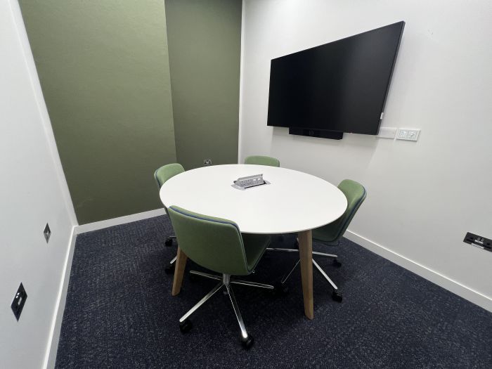 Flat-floored meeting room with round table and chairs, and wall mounted video monitor.