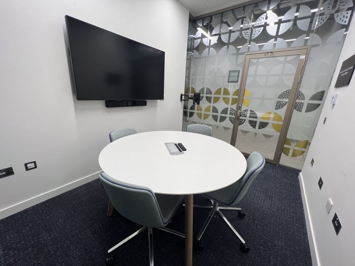 Flat-floored meeting room with round table and chairs, and wall mounted video monitor.