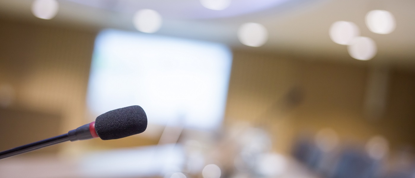 Photo of a microphone at the front of a conference hall with blurred background