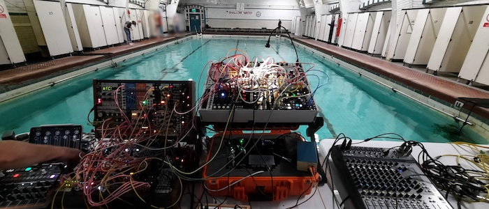 A picture of a modular synthesiser set up at the edge of a swimming pool ahead of a Swimming with Gravitational Waves event