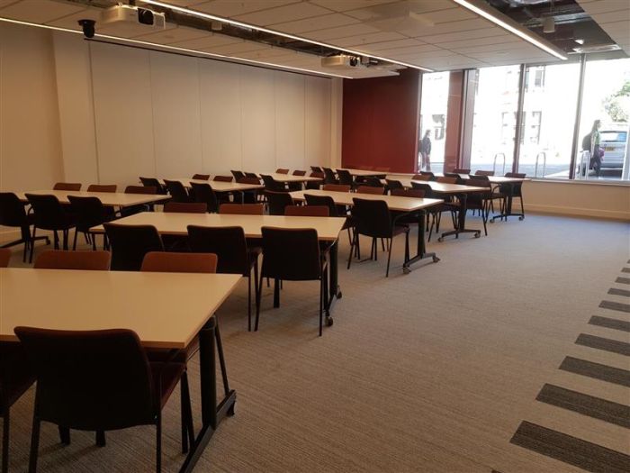 Flat floored teaching room with tables and chairs, and projectors.