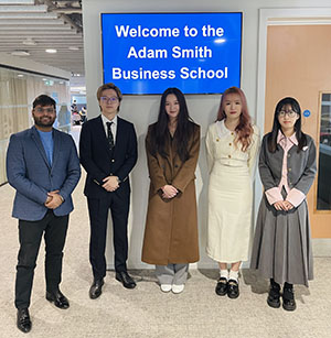 5 students standing in front of a screen saying Adam Smith Business School