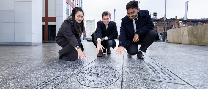 Adam Smith Business School students kneeling down looking at the Adam Smith paving stones at their launch 